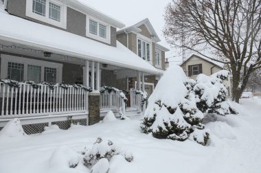 Toronto, ON, Kanada - 27 Şubat 2025: Banliyö evi çatıdan sarkan buz saçaklarıyla kaplı, güneş ışığı beyaz kış manzarasına gölge düşürürken,.