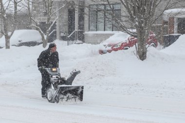 Toronto, ON, Kanada - 27 Şubat 2025: Bir adam varoş mahallesinde yoğun kar yağışı sırasında garaj yolundaki derin karı temizlemek için kar temizleme makinesi kullanıyor.