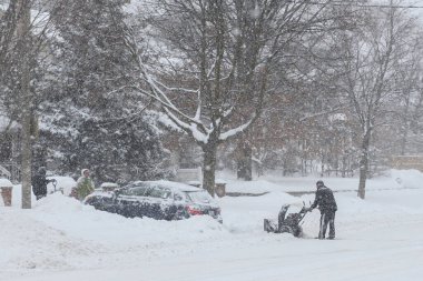 Toronto, ON, Kanada - 27 Şubat 2025: Bir adam varoş mahallesinde yoğun kar yağışı sırasında garaj yolundaki derin karı temizlemek için kar temizleme makinesi kullanıyor.