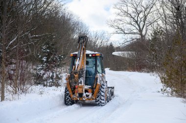 Toronto, ON, Kanada - 27 Şubat 2025: Güvenlik ekipmanlı iki işçiyle kar küreme aracı kar kaplı kırsal bir yolu temizliyor, soğuk bir kış gününde taze karı kenara itiyor.