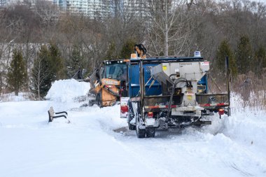 Toronto, ON, Kanada - 27 Şubat 2025: Güvenlik ekipmanlı iki işçiyle kar küreme aracı kar kaplı kırsal bir yolu temizliyor, soğuk bir kış gününde taze karı kenara itiyor.