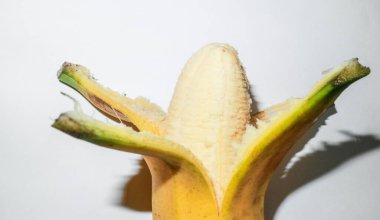 Beyaz arka planda yarısı soyulmuş olgun bir muz. Taze tropikal atıştırmalık ve sağlıklı yiyecek kavramı..