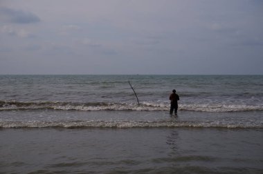 Local man standing beach of wavy sea at daytime, pantai utara jawa, di kota Pemalang, ombaknya kecil, nampak pemancing di pinggir pantai, sedang memancing ikan, di pantai Widuri, Pemalang, Jawa Tengah, Indonesia, pada siang hari mencari ikan laut