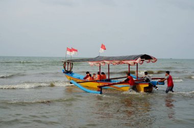 Old boat with local men moving by sea at daytime, perahu nelayan di pinggir pantai Widuri Pemalang, Indonesia, digunakan untuk angkutan wisata laut, wisatawan diajak naik perahu ke tengah laut, ombaknya kecil, resiko kecil membayar sejumlah uang