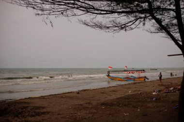 Old boat parked on beach with local people, daytime view, perahu nelayan di pinggir pantai Widuri Pemalang, Indonesia, digunakan untuk angkutan wisata laut, wisatawan diajak naik perahu ke tengah laut, ombaknya kecil, resiko kecil membayar uang 