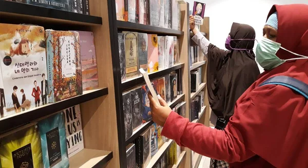 the woman is reading the book. Indonesia, rak buku di toko buku, nampak pengunjung toko buku membaca dan memilih buku yang akan dibeli. budaya membaca buku yang semakin langka dan susah ditemukan, sadar literasi, baik buku ilmiah, pelajaran, novel