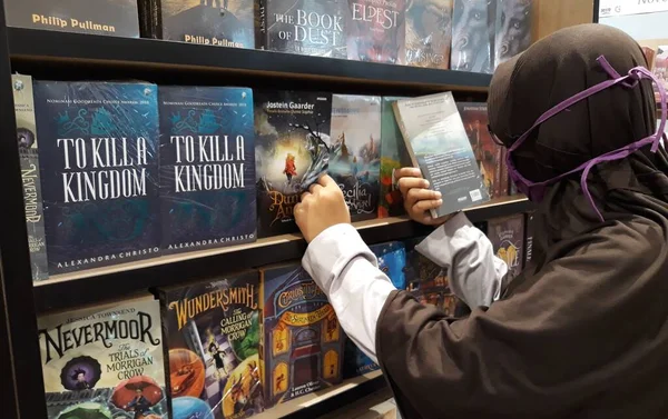 the woman is reading the book. Indonesia, rak buku di toko buku, nampak pengunjung toko buku membaca dan memilih buku yang akan dibeli. budaya membaca buku yang semakin langka dan susah ditemukan, sadar literasi, baik buku ilmiah, pelajaran, novel