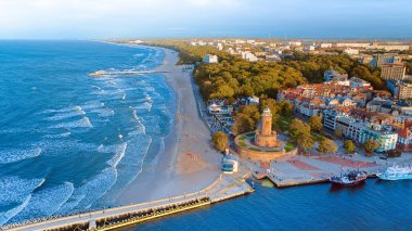 Bu hava görüntüsü Koobrzeg 'in ikonik deniz fenerine ve altındaki gelişen limana odaklanıyor. Bu Polonya mücevherinin deniz atmosferiyle birleşmiş sahil cazibesi çok güzel sergileniyor..