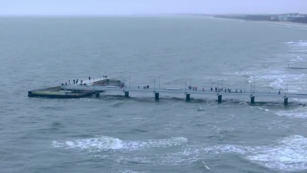 1月のドローン映画では バルト海の海岸線は 遠くのコオブジェグ桟橋で展開しています 人々を巻き込んで 海底を飛び 黄金の砂や嵐の波が冬の海岸を描く — ストック動画