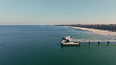 Koobrzeg iskelesinde güneşli bir kış günü. Sakin deniz, dalga yok. İnsanlar gezintiden zevk alıyor..