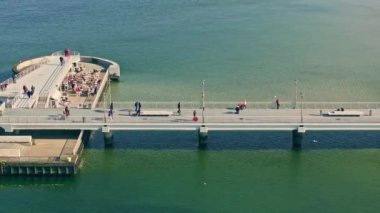 Güneşli bir kış öğleden sonrasında Koobrzeg rıhtımında. Dalgalar yok, turistler geziniyor. Sakin deniz, berrak gökyüzü.
