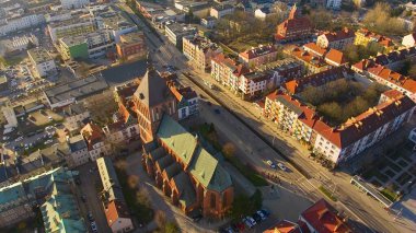 Koszalin şehir merkezini altın ışıkla kaplayan bir drone çekimi, katedralin, Zafer Sokağı ve belediye binasının görüntülerini içeriyor..