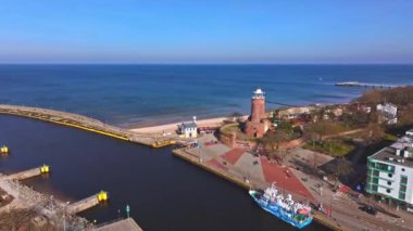 İnsansız hava aracı videosu Kolobrzeg limanının girişini kuş bakışı gösteriyor, bir yolcu gemisi, bir kırmızı tuğlalı deniz feneri ve rıhtımdaki turistleri gösteriyor. Kaydedildi güneşli bir Şubat gününde.