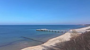 İHA görüntülerinde Kolobrzeg iskelesi, kumlu plajda turistler, mavi gökyüzü ve güneşli bir Şubat günü deniz kuşları görülüyor..