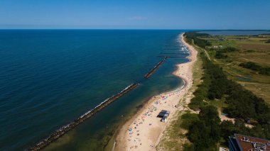 Darowo sahilinin havadan çekilen bir görüntüsünde altın kumlar üzerinde güneşlenenler ve sakin Baltık sularında yüzenler görülüyor. Kıyı otelleri, kumulların tepesinde yoğun bir ormanla sahile bakar ve güzel bir kontrast yaratır..
