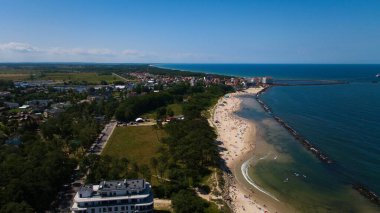 Güneşlenenlerin dinlendiği ve yüzücülerin Baltık Denizi 'nin tadını çıkardığı Darowos' un altın kumlu plajının insansız hava aracı görüntüsü. Gemilerin limandan ayrılıp sakin kıyı manzarasına eklendiği görülebilir. Huzurlu bir deniz ve canlı bir plaj güzel bir yaz günü yaratıyor..