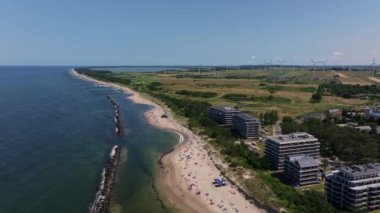 Bir İHA, güneşli bir yaz gününde güneşlenen turistleri ve yüzücüleri gösteren Darowo 'nun kumlu sahillerinde uçuyor. Yakındaki sahil tatil beldeleri ve oteller kıyı şeridi boyunca uzanan doğal kıyı şeridi arasında güzel bir kontrastlık sunuyorlar..