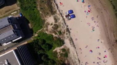 Bir İHA, Darlowo 'nun yaz aylarında Baltık Denizi' nde güneşlenen turist ve yüzücülerle dolu kumlu plajını geniş bir açıdan görüyor. Uzakta, limandan ayrılan gemiler görülebilir ve kıyı şeridinin manzaralı güzelliğine eklenebilir..