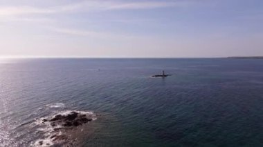 Faro Mangiabarche, Sardinya 'nın sakin mavi denizlerine karşı parlıyor. İnsansız hava aracı, sakin dalgaları ve engebeli kayaları filme alır. Parlak güneş ışığı bu güzel kıyı manzarasını tamamlar..