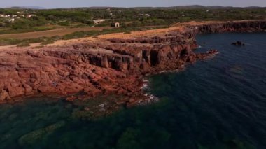 Sant 'Antioco' daki Faro Mangiabarche yakınlarındaki kayalık kıyı şeridi, huzurlu dalgalar ve kahverengiyle mavinin çarpıcı zıtlıklarıyla güneşin altında parlar..