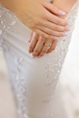 Nazik bir el nazikçe kalçasında durur, parıldayan bir nişan yüzüğüyle süslenir. Pullu beyaz elbise usulca parıldıyor, zerafetin, aşkın ve beklentinin özünü yakalıyor..