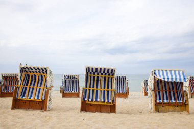 Kolobrzeg 'in geniş kumlu plajında, beyaz-mavi çizgili vintage ahşap ve hasır sepetler plaja gidenler için gölge sağlar. Baltık Denizi ve ağustos ayının sakin bulutları güzel bir kıyı manzarası yaratır..