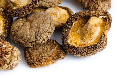 Beyazın üzerindeki kurumuş shiitake mantarlarının yakın plan bir resmi, doğal, kırsal cazibe ve gurme kalitesini vurgulayarak, detaylı dokuları ve zengin toprak renklerini vurgular..