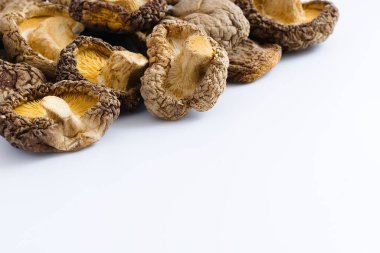 Bu canlı görüntü, geleneksel bir mutfak malzemesinin orijinalliğini sembolize ederek, kaba dokularını ve zengin toprak tonlarını yakalayan, beyaz üzerinde kurutulmuş shiitake mantarları barındırıyor..