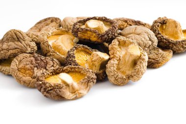 Beyaz bir zemin üzerinde kurumuş shiitake mantarlarının sanatsal yakın çekimi karmaşık dokularını ve derin doğal renklerini sergiliyor. Gurme için mükemmel, organik besin tasvirleri..