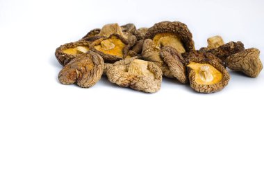 Kurumuş shiitake mantarlarının beyaz üzerine sanatsal bir kompozisyonu, onların karmaşık dokularını ve derin doğal tonlarını vurgular ve izleyicileri kırsal güzelliklerini ve aşçılık potansiyellerini takdir etmeye davet eder..