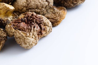 Kurutulmuş Şiitake mantarları, geleneksel mutfak mirasına hitap eden karmaşık, kırsal dokularını ve zengin, tuzlu renklerini vurgulayan el değmemiş beyaz bir yüzeyde güzelce sergilenir..