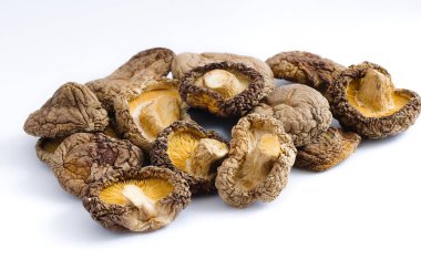 El değmemiş beyaz bir arka planda ustaca düzenlenmiş, kurutulmuş shiitake mantarları karmaşık dokularını ve derin umami renklerini sergiliyor, geleneksel mutfak malzemelerini takdir etmeye teşvik ediyor..