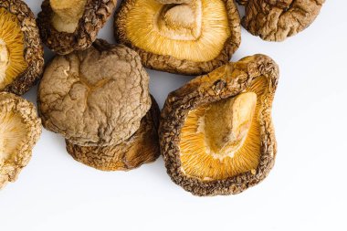 Kurutulmuş shiitake mantarları temiz beyaz bir zemin üzerine sergilenir. Karmaşık dokuları ve derin doğal renkleri onları mutfak ve doğa temalı görseller için mükemmel bir konu yapar.