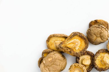 Beyaz bir zemin üzerinde kurumuş shiitake mantarlarının yakın plan görüntüsü, bu geleneksel, umami paketlenmiş bileşenin özünü yakalayarak, toprak kahverenginin her kırışıklığını ve tonunu ortaya çıkarır..