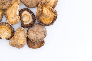 Kurutulmuş Şiitake mantarları, geleneksel mutfak mirasına hitap eden karmaşık, kırsal dokularını ve zengin, tuzlu renklerini vurgulayan el değmemiş beyaz bir yüzeyde güzelce sergilenir..