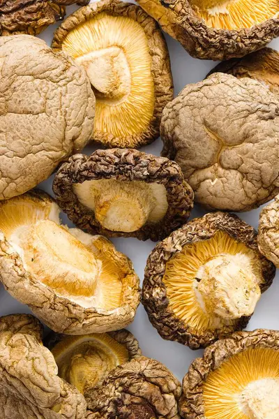Saf beyaz arka planda, kurutulmuş shiitake mantarları sanatsal bir düzende sergilenir, engebeli dokuları ve derin umami tonları aşçılık geleneğine bir bakış sunar..