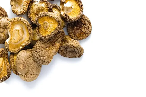 Bu resim, hem geleneği hem de sofistike mutfağı çağrıştıran, detaylı dokuları ve derin toprak tonlarıyla beyaz bir zemin üzerinde zarif bir şekilde düzenlenmiş kurutulmuş shiitake mantarlarını içeriyor..