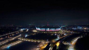 Varşova 'nın ışıldayan siluetini geceleyin bir dron yakalıyor. PGE Narodowy, Switokrzyski Köprüsü ve sonsuz şehir ışıkları Wisa Nehri' ne yansıyor..