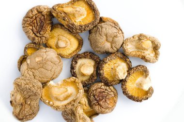 Bu resim özenle düzenlenmiş beyaz bir zemin üzerinde kurutulmuş shiitake mantarlarını, eşsiz dokularını ve doğal zarafetle harmanlanmış sade renkleri sergiliyor..
