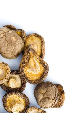 Kurumuş shiitake mantarlarının beyaz üzerine sanatsal bir kompozisyonu, onların karmaşık dokularını ve derin doğal tonlarını vurgular ve izleyicileri kırsal güzelliklerini ve aşçılık potansiyellerini takdir etmeye davet eder..