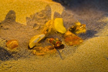 Kolobrzeg 'de yaz günbatımı Kum üzerinde uzanan kehribar taşlarını aydınlatır, altın saat sükunetinde sıcak bir şekilde parlar.