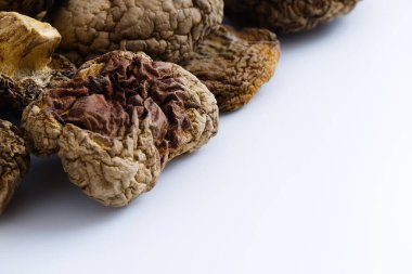 Kurumuş shiitake mantarlarının beyaz üzerine sanatsal bir kompozisyonu, onların karmaşık dokularını ve derin doğal tonlarını vurgular ve izleyicileri kırsal güzelliklerini ve aşçılık potansiyellerini takdir etmeye davet eder..