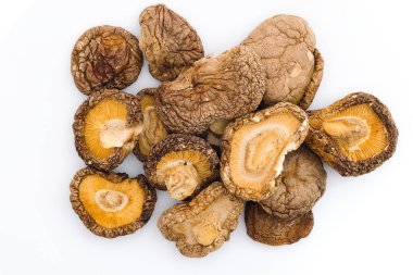 Çarpıcı bir görüntü beyaz arka planda kurumuş shiitake mantarlarını gösteriyor, onların engebeli dokularını ve doğal yemek pişirme geleneğini anlatan derin organik renkleri vurguluyor..