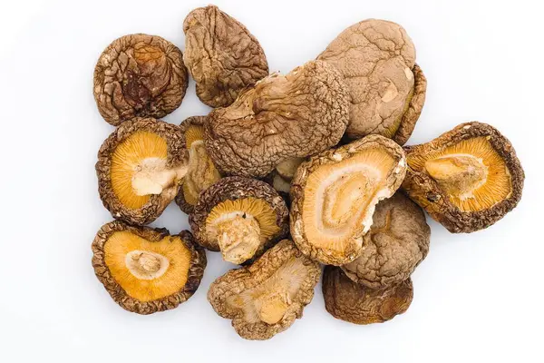 Çarpıcı bir görüntü beyaz arka planda kurumuş shiitake mantarlarını gösteriyor, onların engebeli dokularını ve doğal yemek pişirme geleneğini anlatan derin organik renkleri vurguluyor..