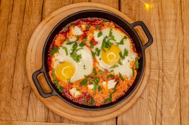 Beyaz seramik tabakta yumurta ve peynirli omlet ve ahşap arka planda sebzeler.