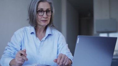 Kadın sekreter iş yazışmalarını dizüstü bilgisayarında tutuyor, not defterine notlar yazıyor.