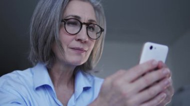 Şık gözlüklü çekici kadın akıllı telefondan sosyal ağlarda sohbet ediyor.