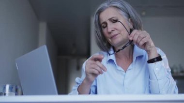 Üst düzey gri saçlı kadın gözlük takıyor ve dizüstü bilgisayarda çalışmaya başlıyor. Belgeler yazıyor. Online dergi için yeni bir makale üzerinde çalışan kadın editör.