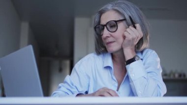 Çevrimiçi sohbetin olgun kadın operatörü dizüstü bilgisayara bakıyor ve esniyor, yorgunluk hissediyor bilgisayarda çalışıyor, uyumak istiyor, fazla çalışıyor, gece vardiyası yapmak istiyor.