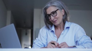 Ciddi bir bayan patron, gri saçlı, internetten görüşme yapıyor. Boş yer için başvuranlarla iletişim kuruyor. Ofisindeki bilgisayarında web kamerası kullanıyor.